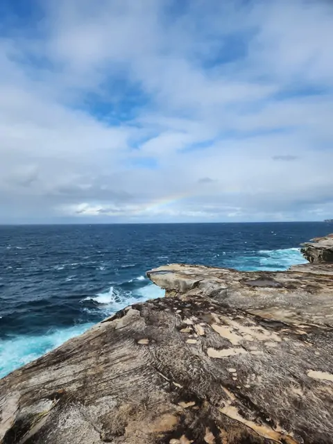 A rainbow stretching over the blue ocean and rocky cliffs.