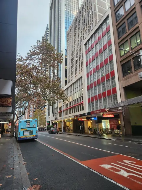 A blue bus driving past red-patterned skyscrapers in the city center.