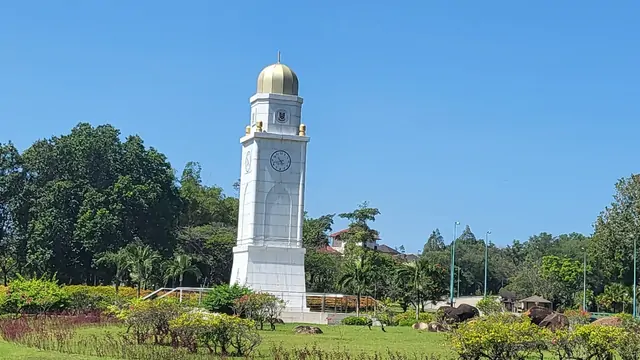 The historic clock tower surrounded by green parkland in the daylight.