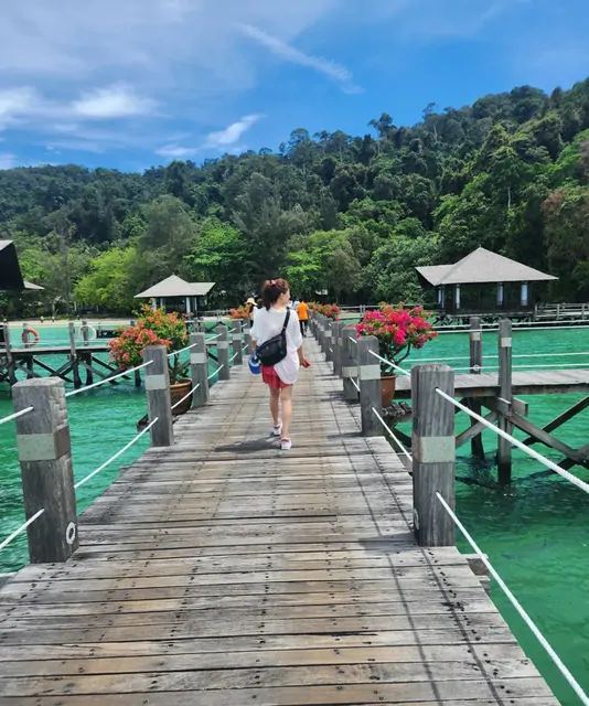 Walking along a wooden jetty toward overwater bungalows in emerald water.