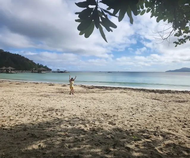 A child cheering on an emerald beach near a water resort.