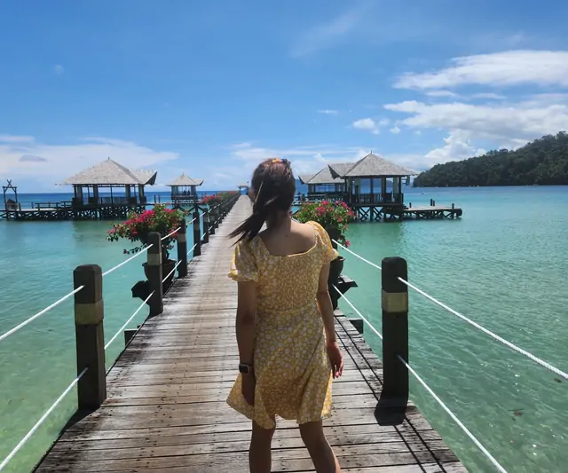 A woman in a yellow dress on the deck of an overwater bungalow.