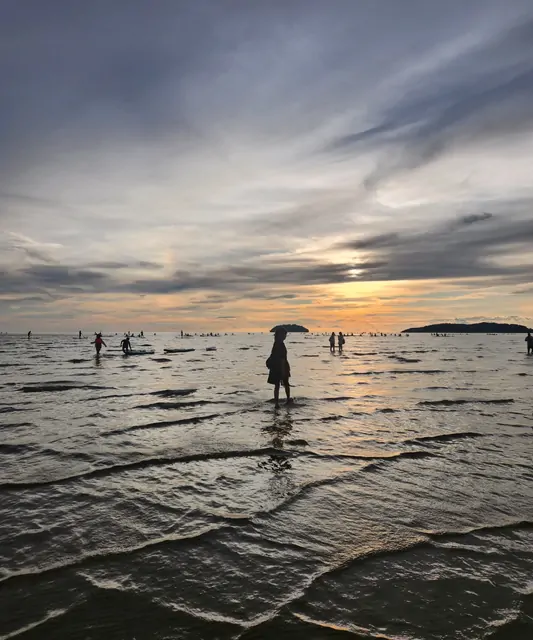 A silhouette of a person with an umbrella standing in the sunset tide.