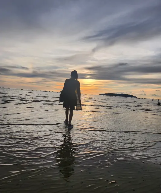 A woman walking along the beach at dusk with a distant island on the horizon.