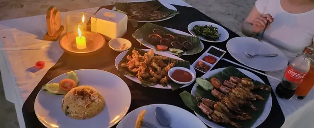 A seafood dinner with fried rice served on banana leaves by candlelight.