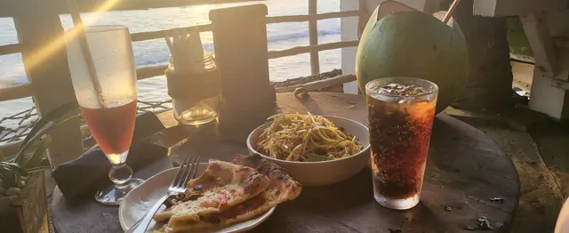 Pizza, papaya salad, and a coconut during a beachside sunset.