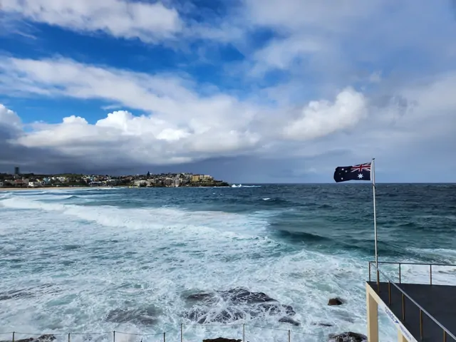 The Australian flag flying near the turbulent waters of Bondi Beach.