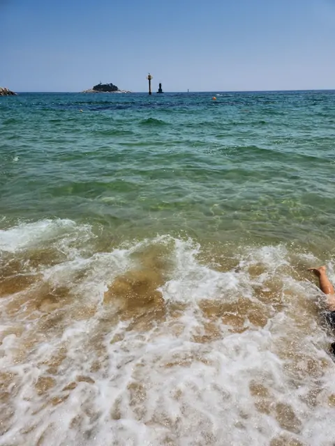 Emerald waves crashing on a summer beach with a distant lighthouse.