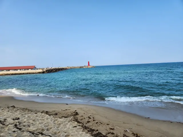 A red lighthouse and breakwater on a quiet beach.