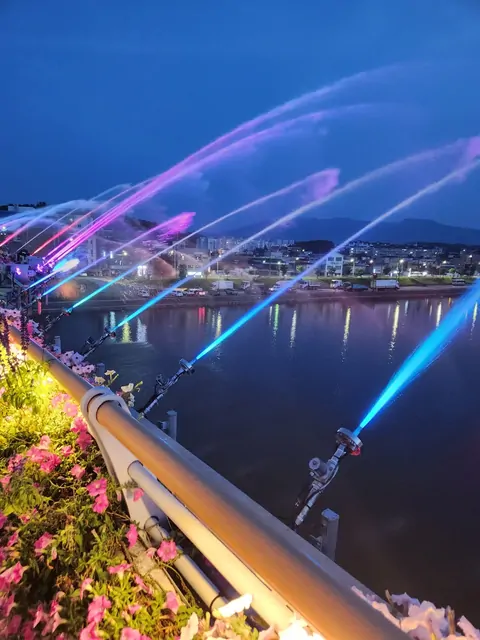 A colorful laser fountain show by the river at night.
