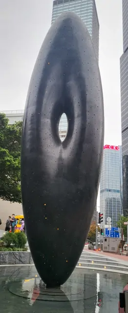 A large black oval sculpture standing in a modern city plaza.