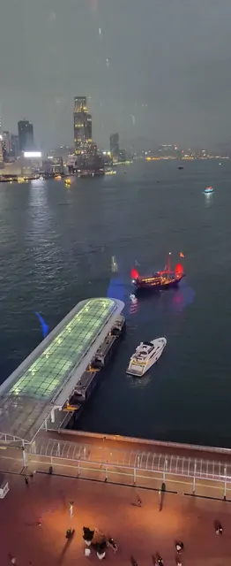 A red-sailed junk boat contrasting with the glowing city skyline.