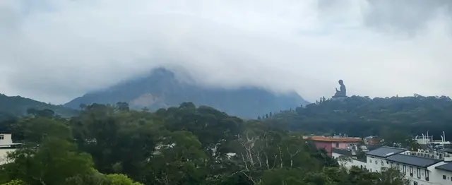The Tian Tan Buddha standing tall above the clouds and forest.