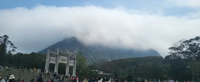 Visitors gathering at the Po Lin Monastery plaza under a cloudy sky.