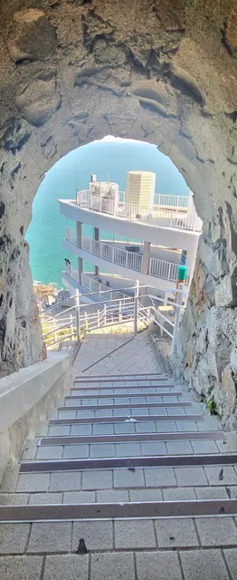 A view of coastal cliffs and stairs framed by a natural rock tunnel.