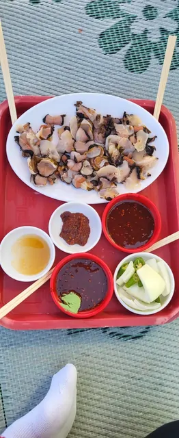 Fresh sea cucumber and shellfish served with sauces on a red tray.