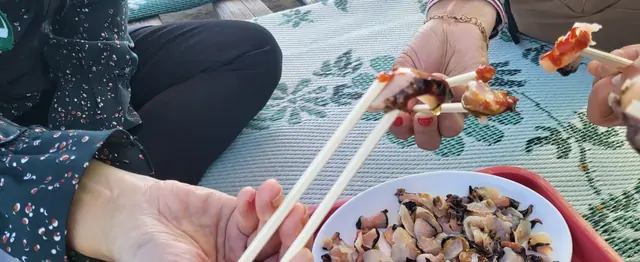 Enjoying a seafood picnic on a mat spread across the ground.