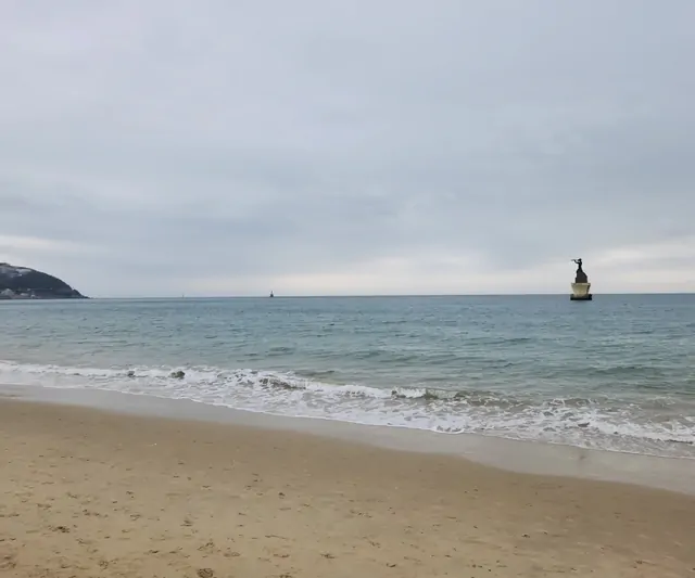 Calm waves washing over the sandy shores of Haeundae Beach on a cloudy day.