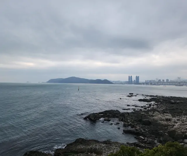 A distant view of Gwangalli and Marine City skyscrapers from the rocky shore.