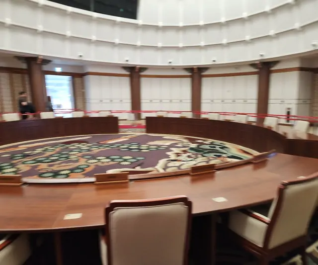 A formal circular meeting room with a large round table and ornate carpet.