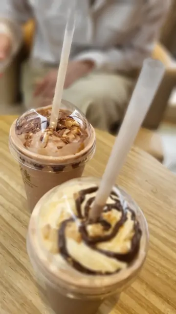 Chocolate frappuccinos with cream on a wooden cafe table.