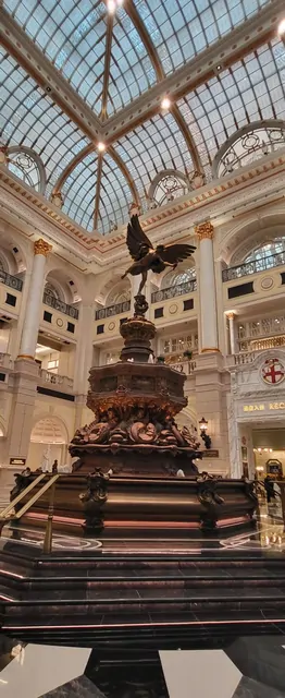 An eagle sculpture under a glass ceiling in a classic European-style mall.