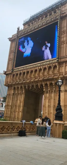 Tourists standing before a large LED screen and Gothic walls at One Central Square.