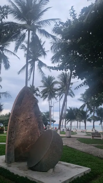 A large stone sculpture standing in the beach park among the palms.