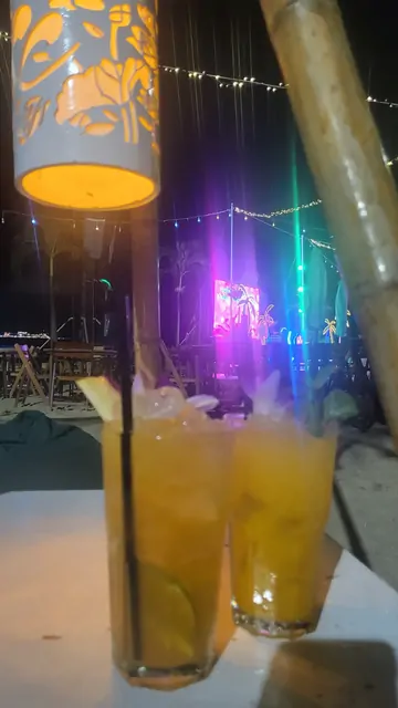 Two tropical cocktails at an outdoor beach bar with a stage in the background.