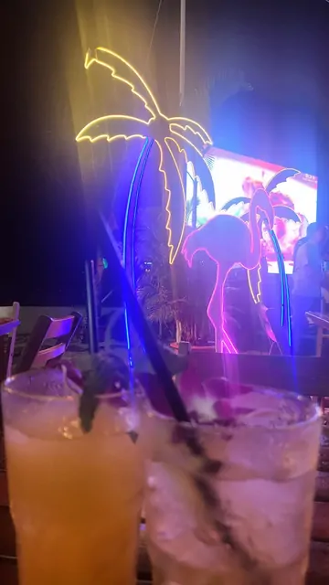 Cocktails placed in front of glowing neon decorations at night.
