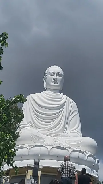A massive white Buddha statue towering over visitors under a grey sky.
