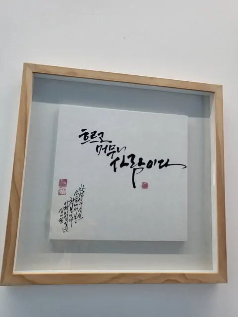 Korean calligraphy in a wooden frame reading 'Flowing and staying, it is love'.