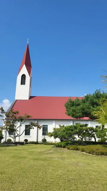 A church with a red roof and white spire against a bright blue sky.