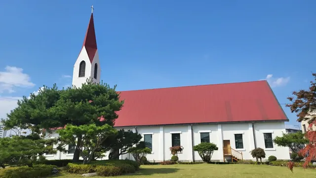 The small red-roofed church situated within a green grass garden.