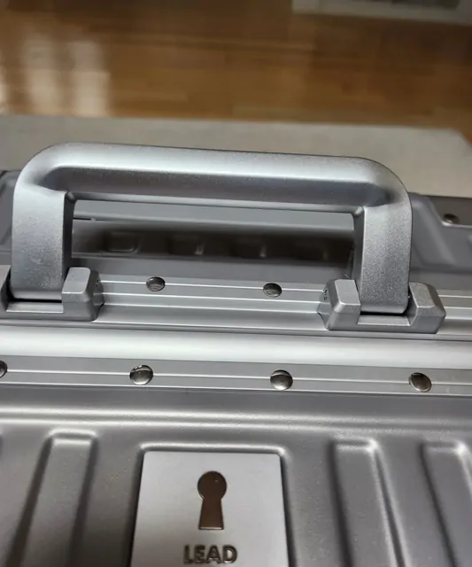 Close-up of the lock and handle of a silver aluminum suitcase.
