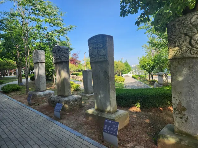 Outdoor display of ancient stone monuments among green trees.