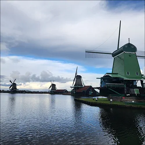 Green wooden windmills reflected in the calm waters of Zaanse Schans.