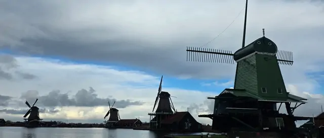 A row of traditional windmills under a heavy, overcast sky.