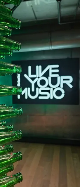 Neon 'LIVE YOUR MUSIC' sign and green bottle installation in a modern bar.