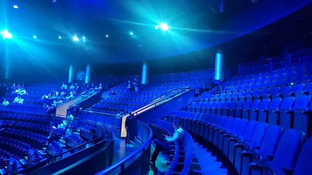 The serene blue lighting and curved seating of a large concert hall.