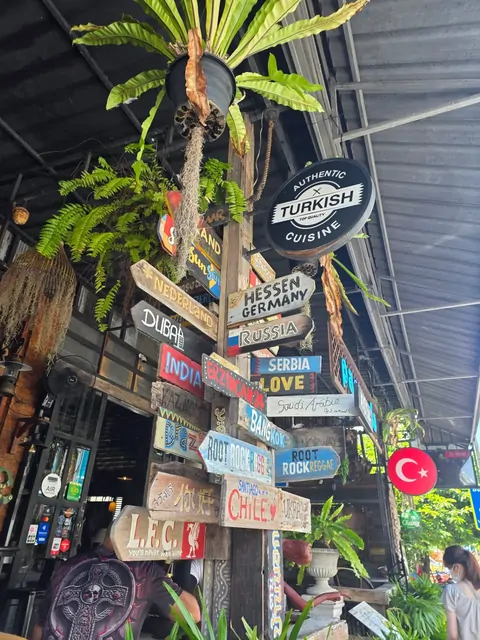 A colorful signpost with global city names in front of a Turkish restaurant.