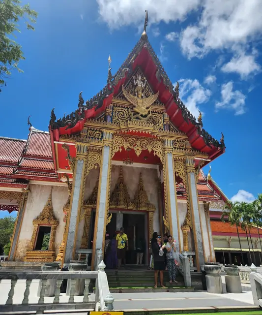 Tourists standing before the golden decorated gate of a temple.