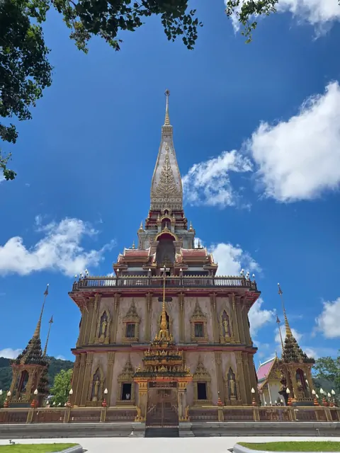 The towering golden spire of Wat Chalong against a blue sky.