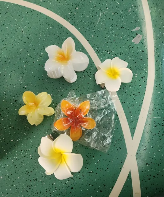 Plumeria flower hairpins resting on a green terrazzo table.